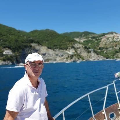 An Akhir Cruise skipper in a white cap at the bow, with the Amalfi Coast behind
